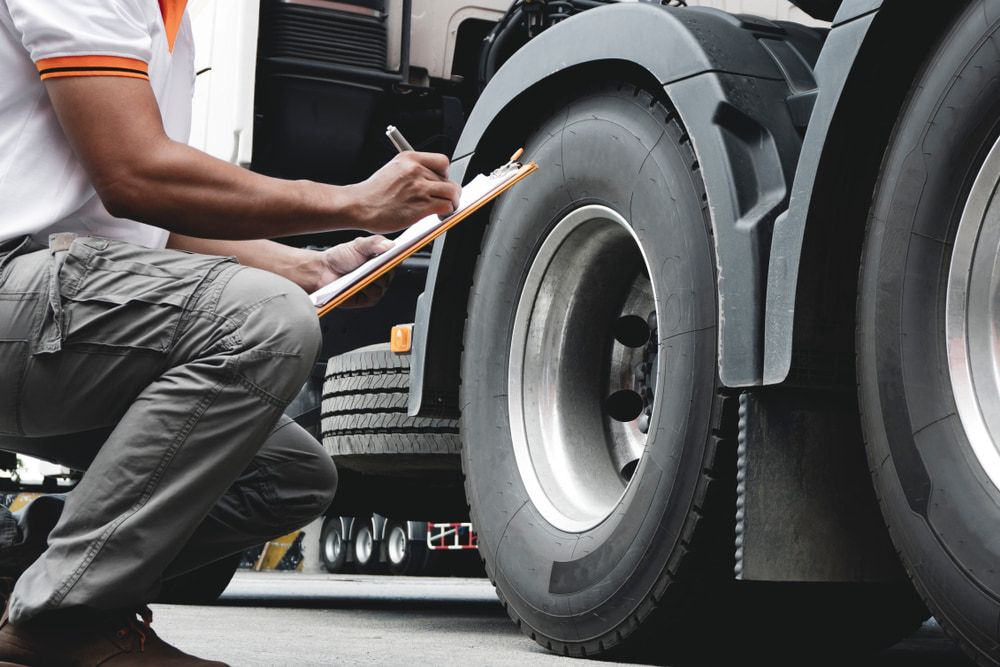 A Man is Kneeling Down Next to a Truck and Writing on a Clipboard — Bowen Mechanical & Haulage in Bowen, QLD
