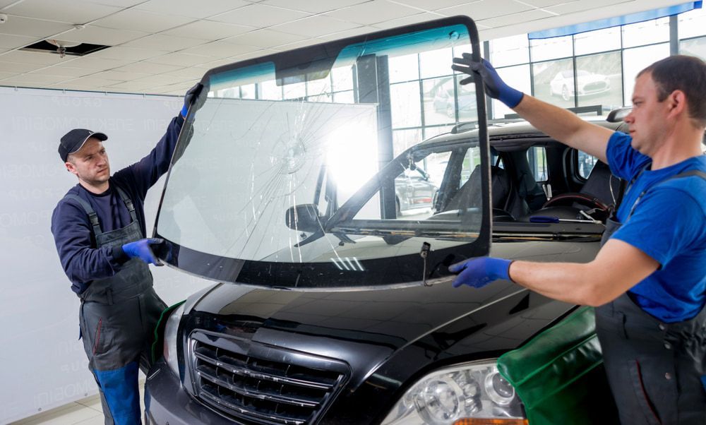 Two Men Are Installing a Windshield on a Car — Bowen Mechanical & Haulage in Bowen, QLD