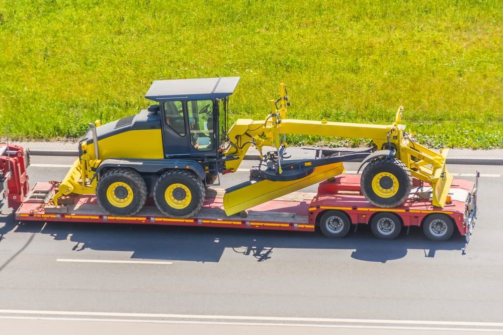 A Yellow Tractor is Being Transported on a Trailer on a Highway — Bowen Mechanical & Haulage in Bowen, QLD