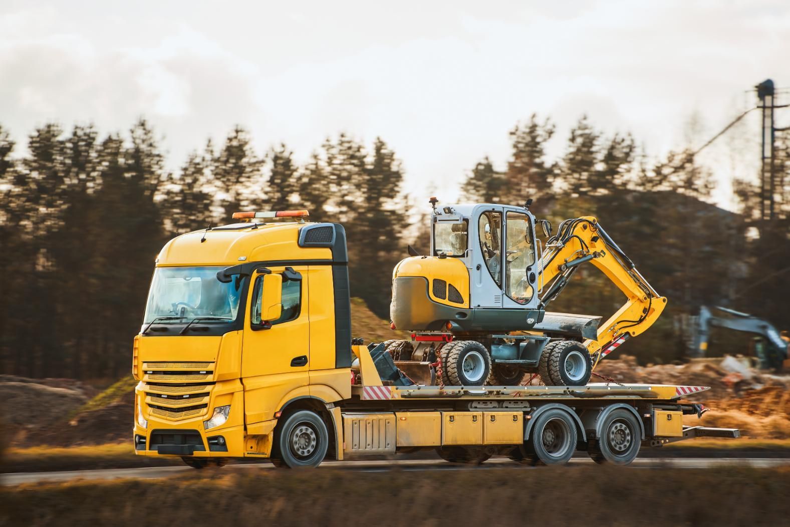 A Yellow Tow Truck is Carrying a Small Excavator on the Back of It — Bowen Mechanical & Haulage in Bowen, QLD