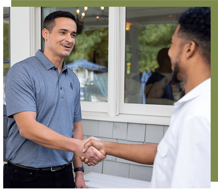 Two men shake hands outside a building. The man on the left wears a blue polo, the man on the right wears a white shirt.