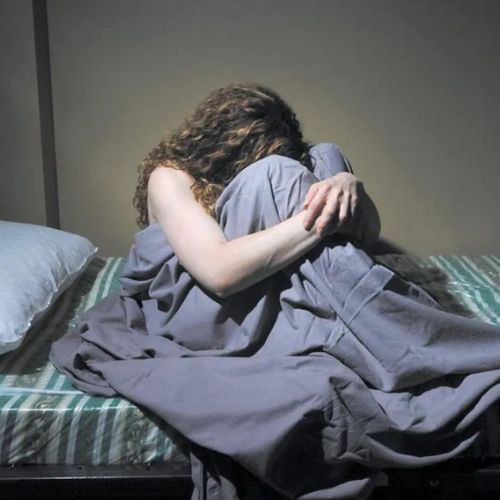 A woman is sitting on a bed with her head in her hands