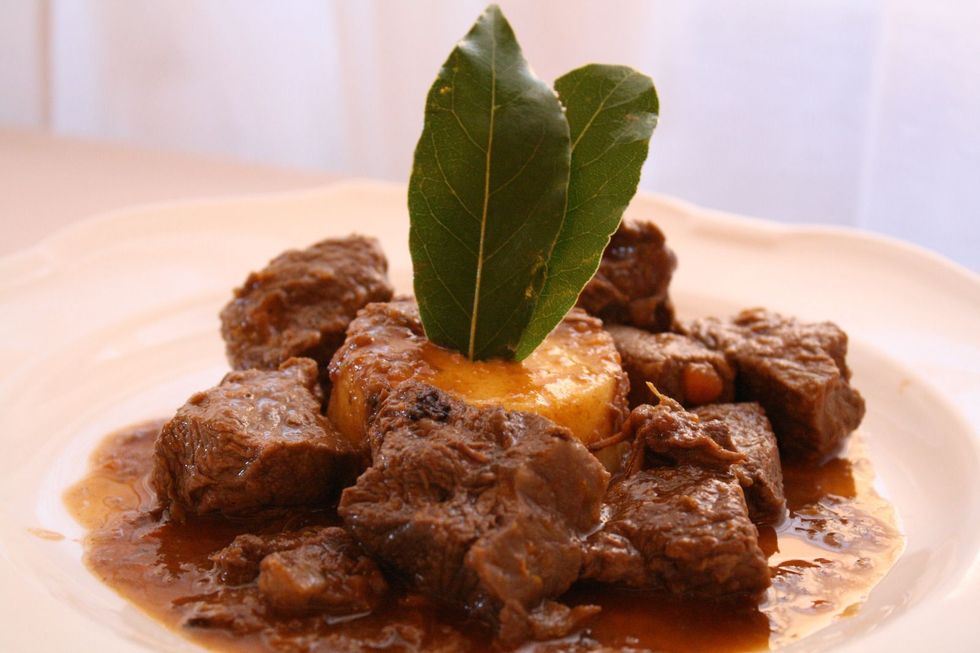 Spezzatino di carne brasata guarnito con foglie di alloro su un piatto bianco, in luce calda