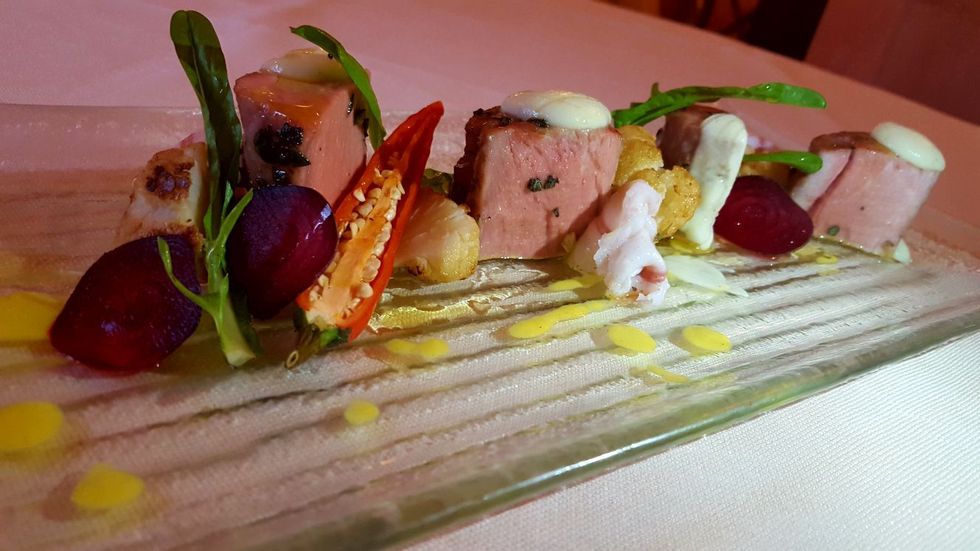 Antipasto gourmet servito su un piatto bianco con verdure, salsa e piccoli spiedini.