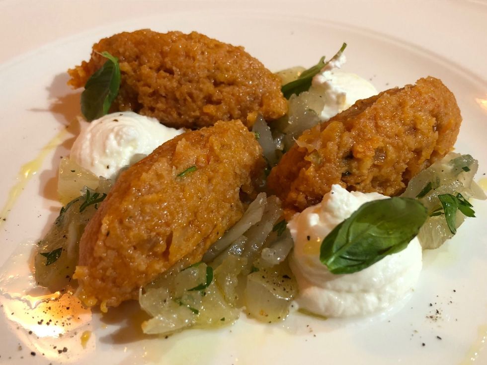 Crocchette fritte servite su un piatto bianco con salsa cremosa, erbe aromatiche e verdure saltate.