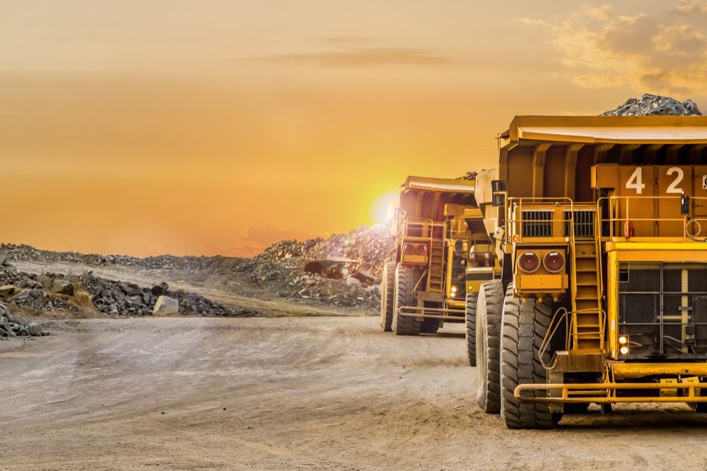 A Row of Dump Trucks Are Parked in A Dirt Field at Sunset — PBC Compliancing in Dysart, QLD