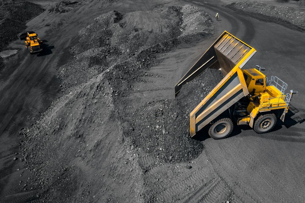 A Yellow Dump Truck Is Driving Down a Dirt Road in A Coal Mine — PBC Compliancing in Rockhampton, QLD