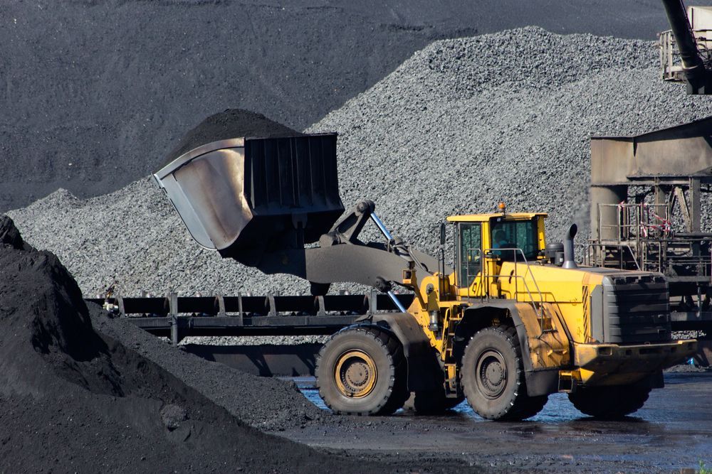 A Yellow Bulldozer is Loading Coal Into a Truck — PBC Compliancing in Townsville, QLD