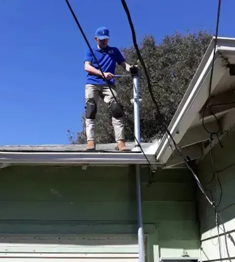Person on a roof near power lines, installing or repairing something. Sunny day.