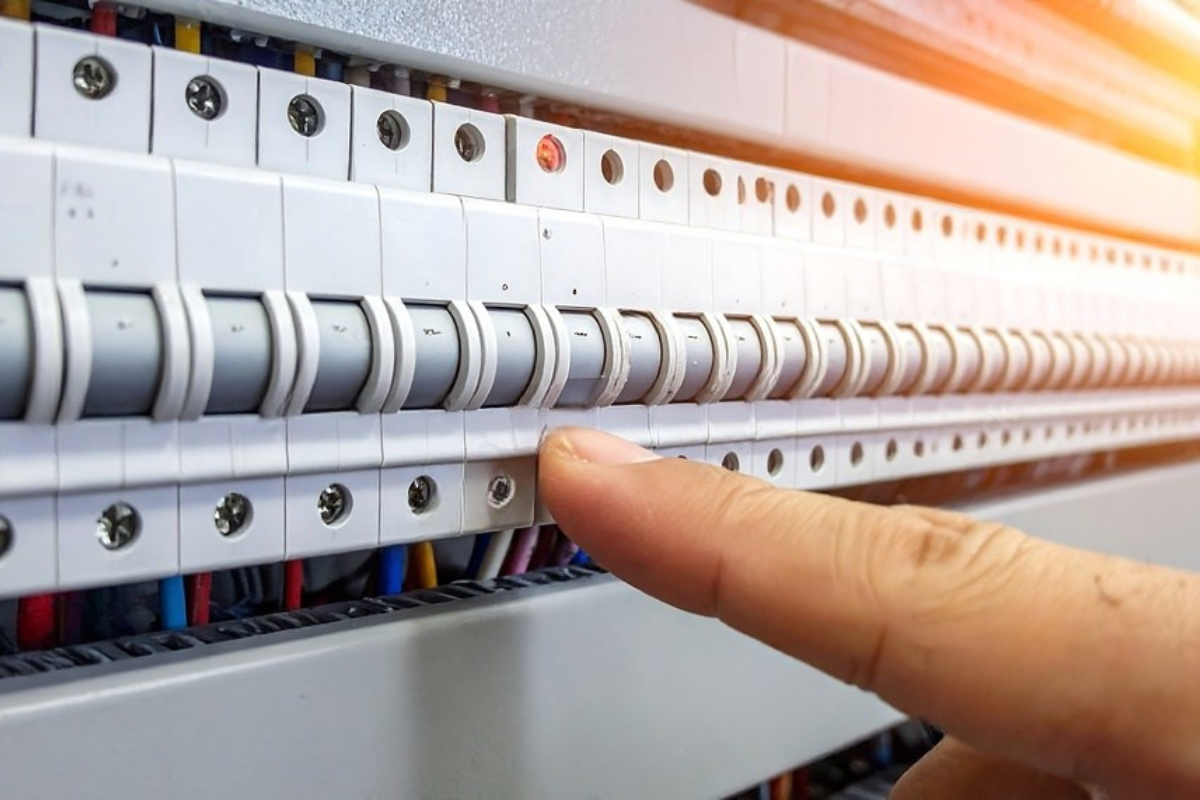 Hand flipping a circuit breaker switch in an electrical panel, with colorful wires visible.