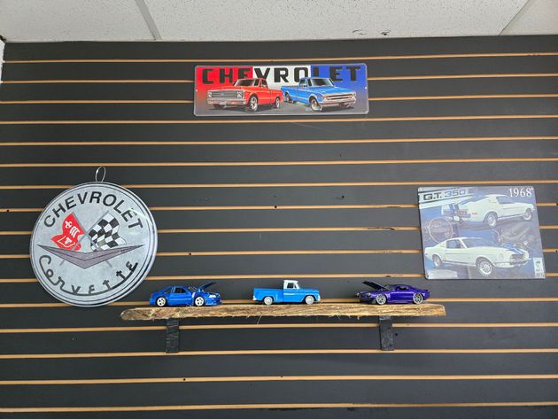 Hot Wheels display wall with three toy cars on a shelf and a Chevrolet sign above