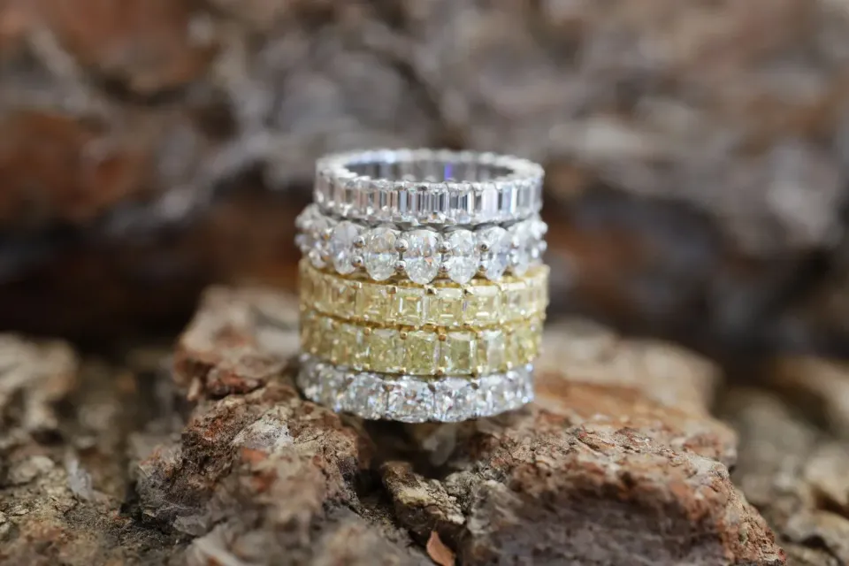 Stacked silver, gold, and white gemstone rings on a rocky surface.
