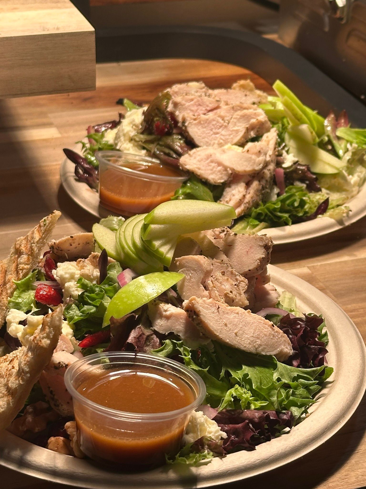Two salads on plates with chicken, apples, and dressing.