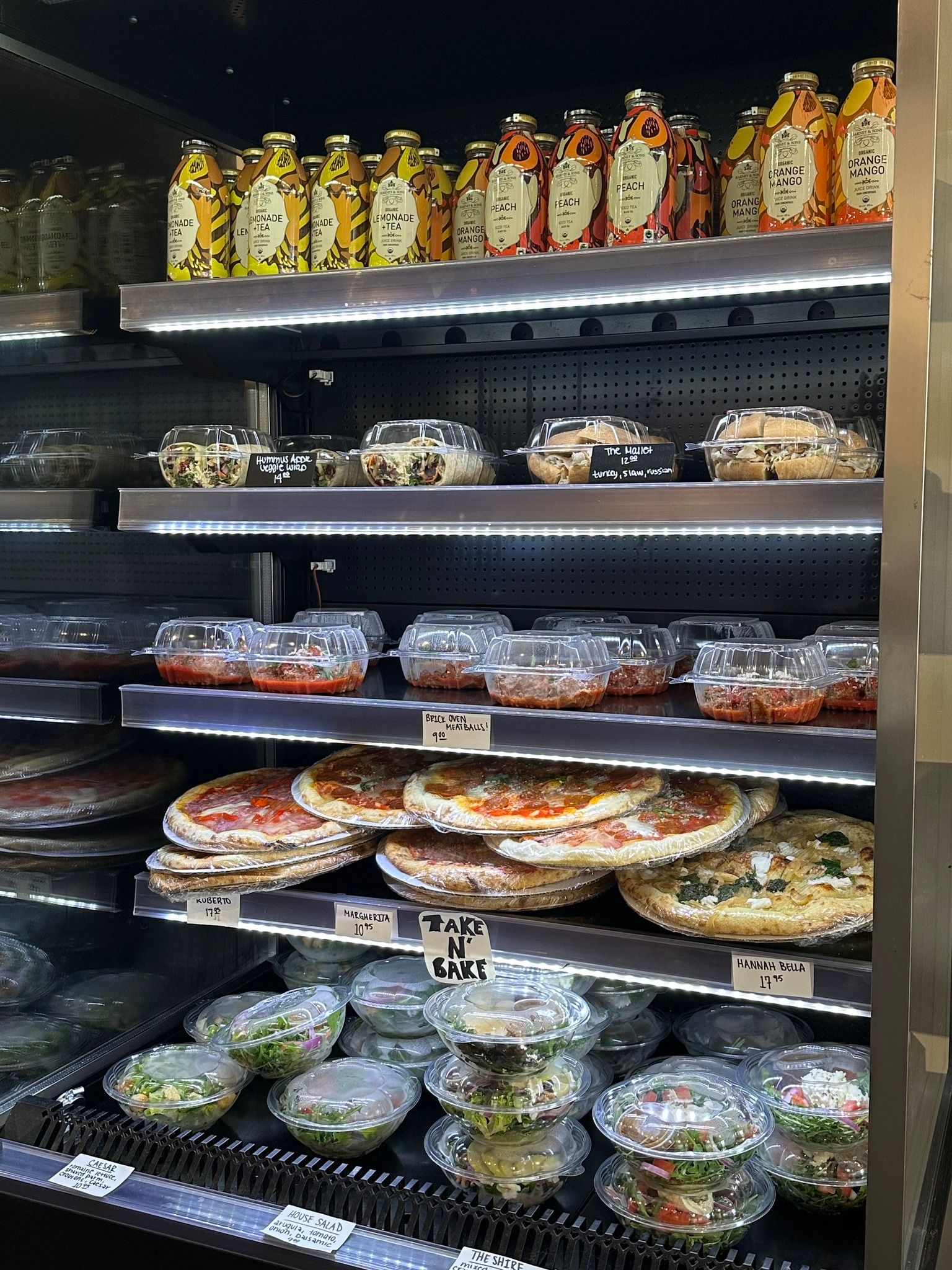 Refrigerator display with prepared foods: pizza, salads, and bottled beverages.