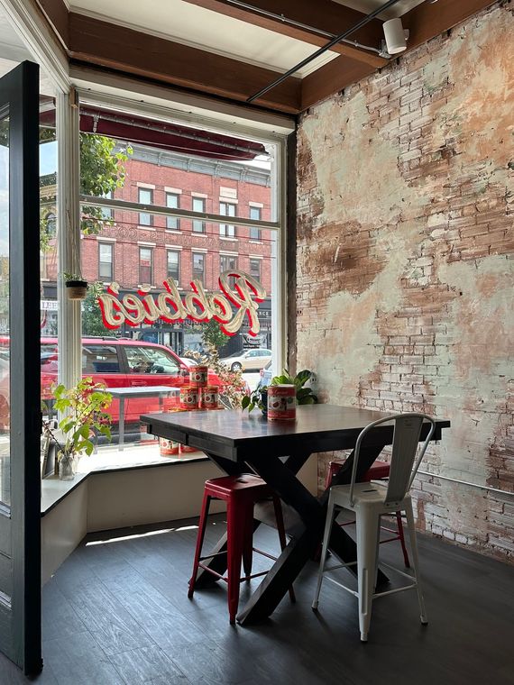 Interior corner dining area with a window view of a city street and exposed brick wall.