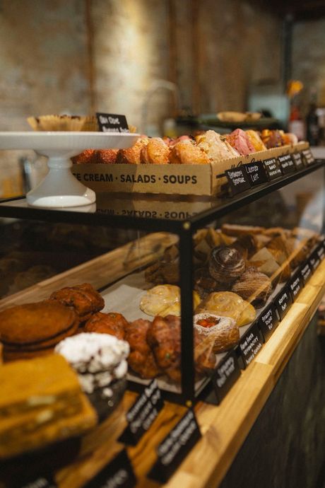 Bakery display case with pastries like croissants and muffins. Wooden shelves and glass.