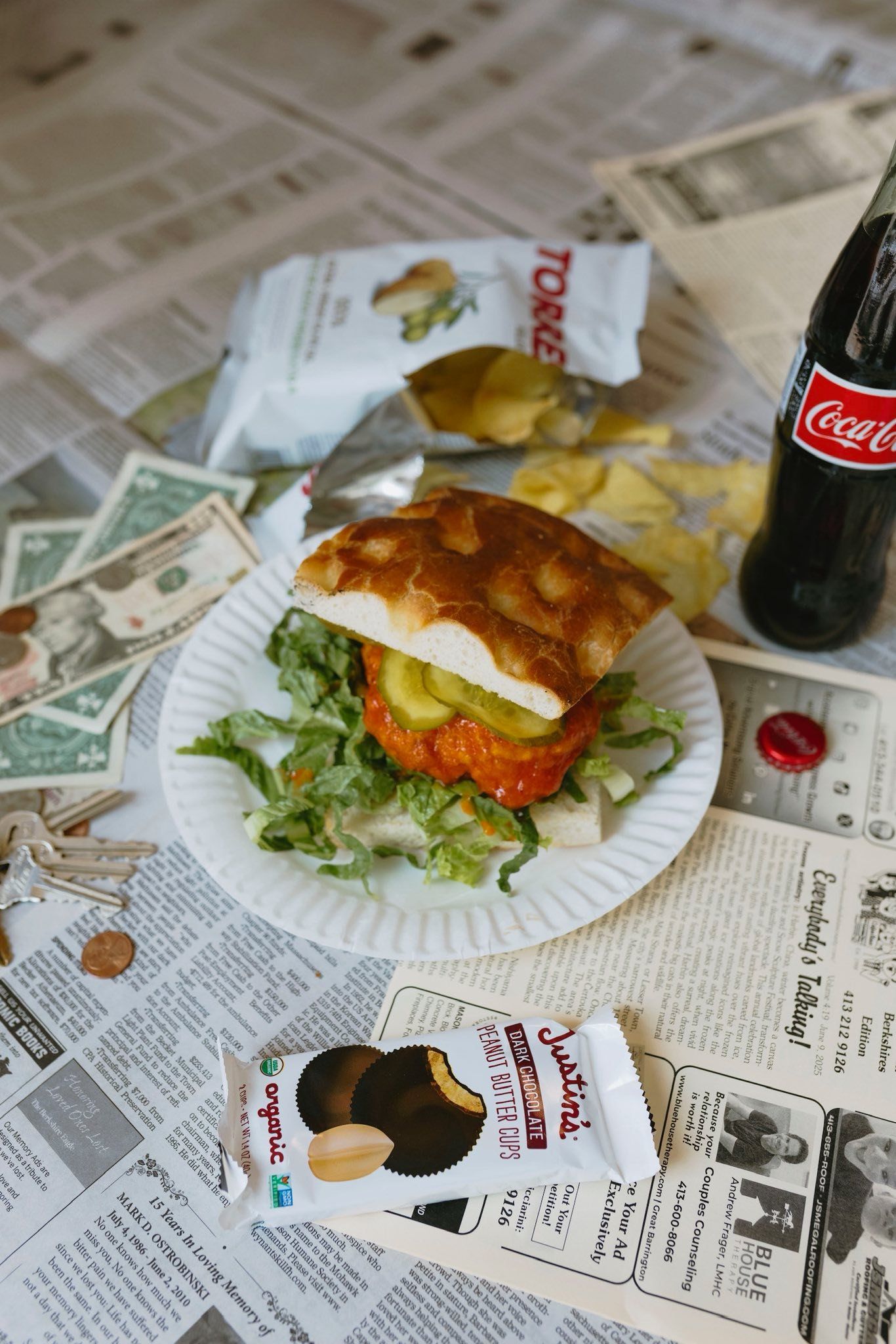 Burger, chips, and Coke on a newspaper-covered surface with money and a cookie.