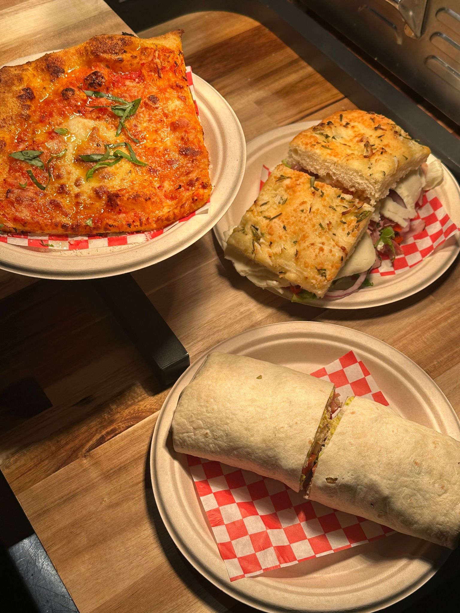 Three dishes of food on disposable plates, including focaccia and a wrap.