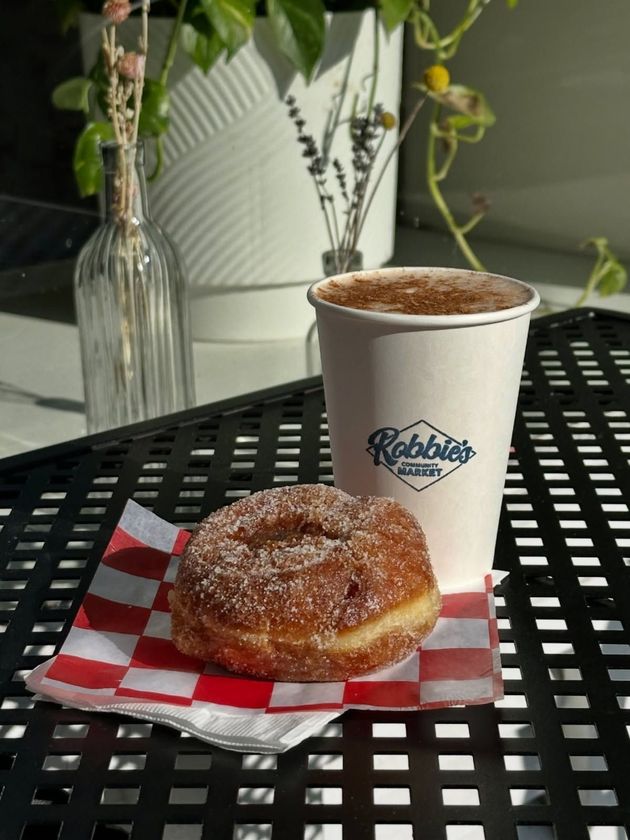 Donut on red and white checkered paper with a coffee cup and floral arrangement on a black table.