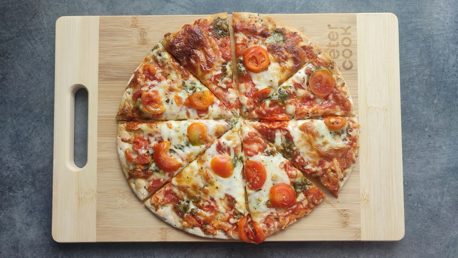 Sliced pizza with tomatoes on a wooden cutting board.