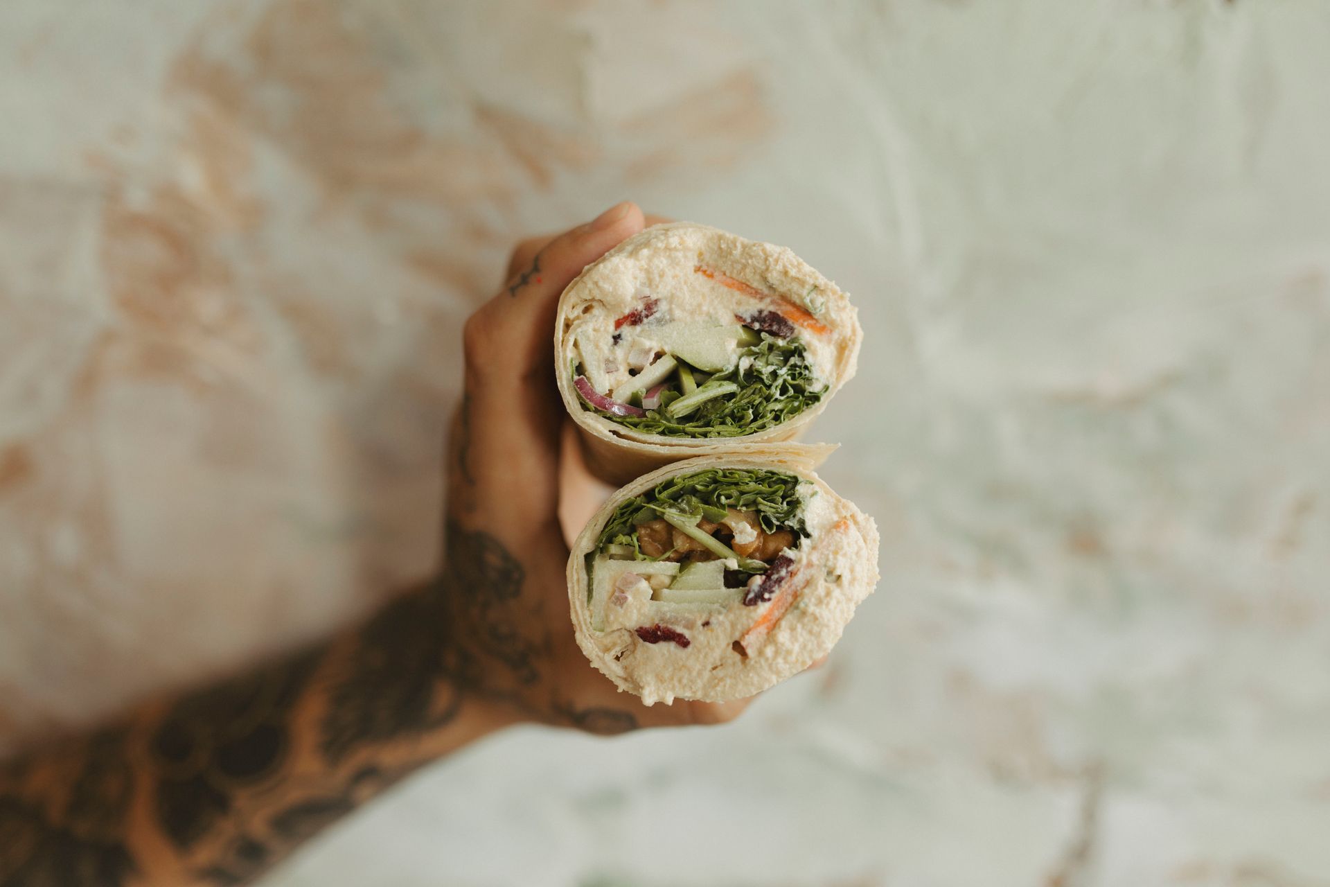 Hand holding a wrap cut in half, revealing fillings of vegetables and sauce.