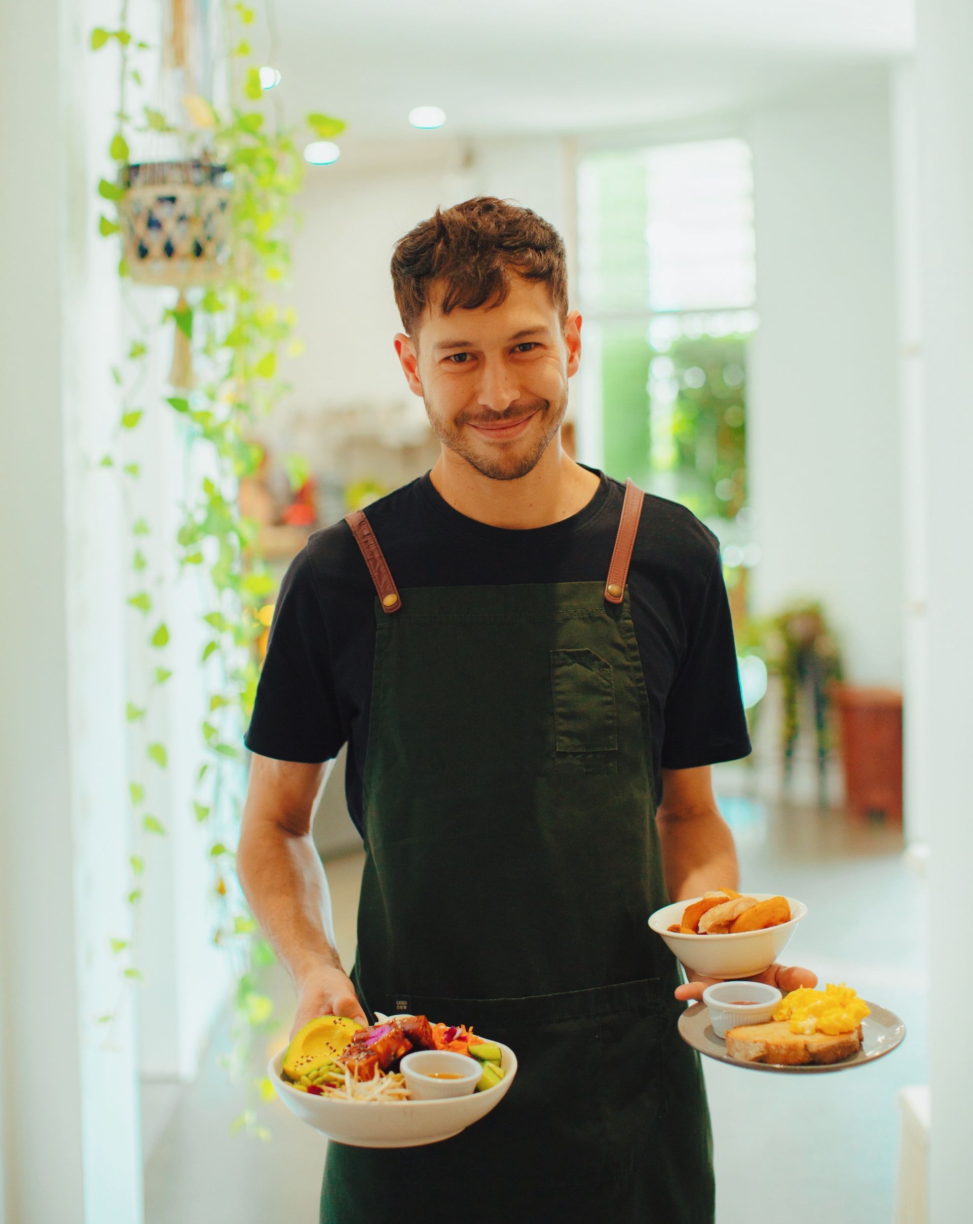 A man in an apron is holding two plates of food.