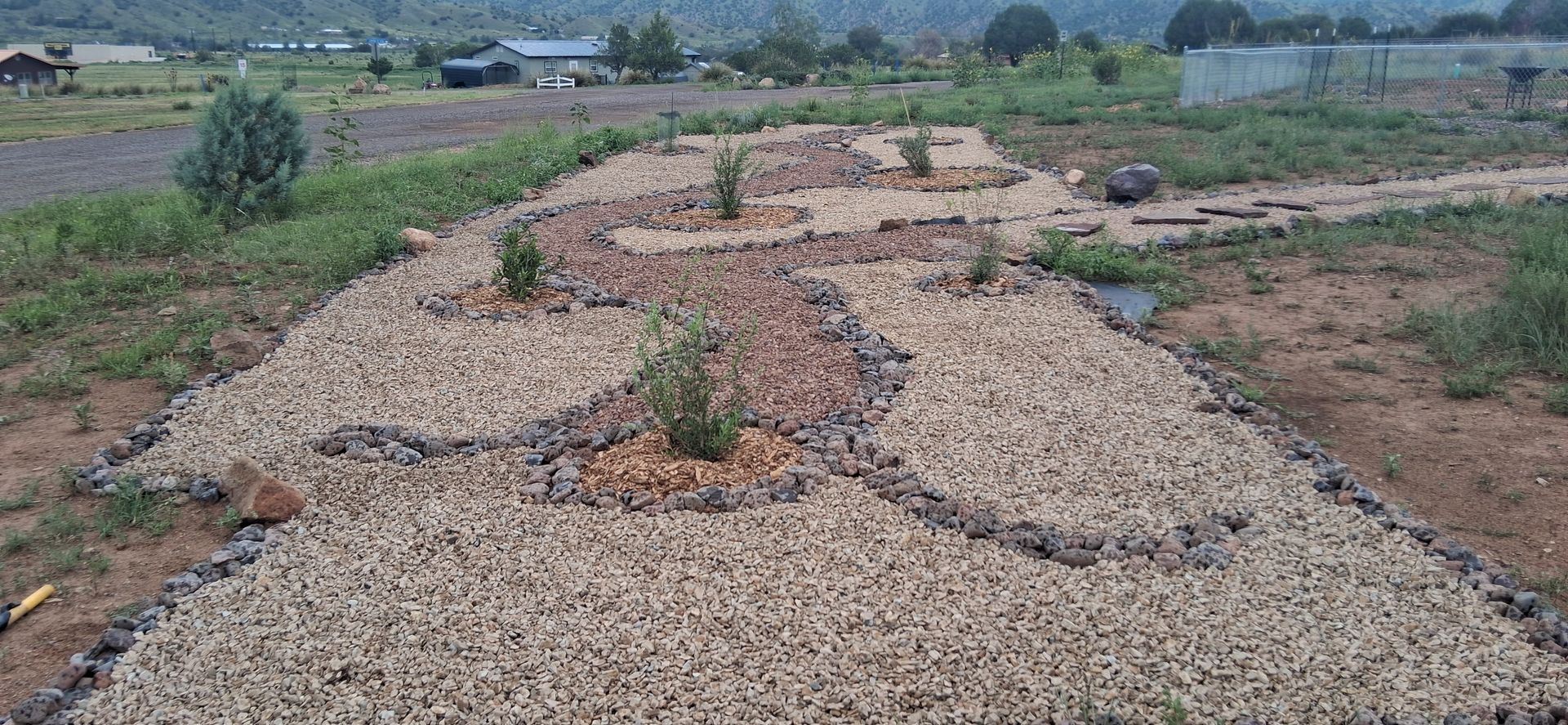 Gravel path winding through a rural field with scattered plants and distant hills