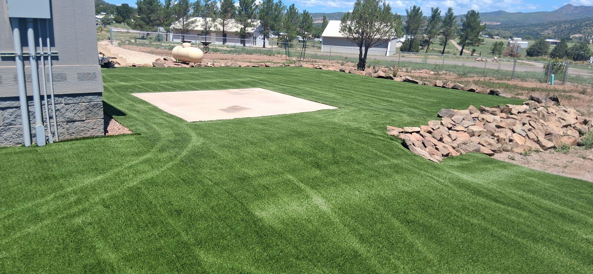 Freshly laid green lawn beside a house, with a concrete pad and dirt piles in a suburban yard