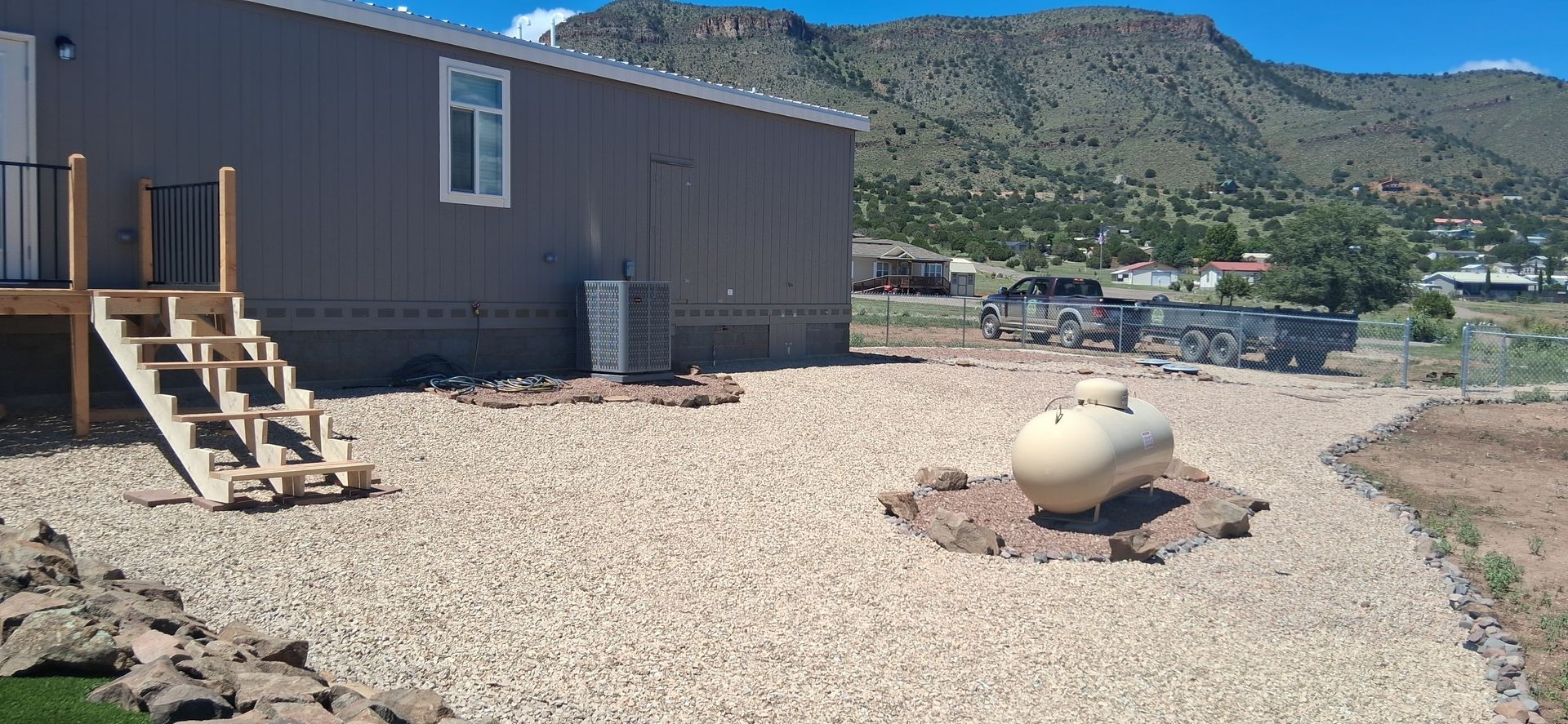 Small gray house with wooden steps and gravel yard, with mountains in the background.