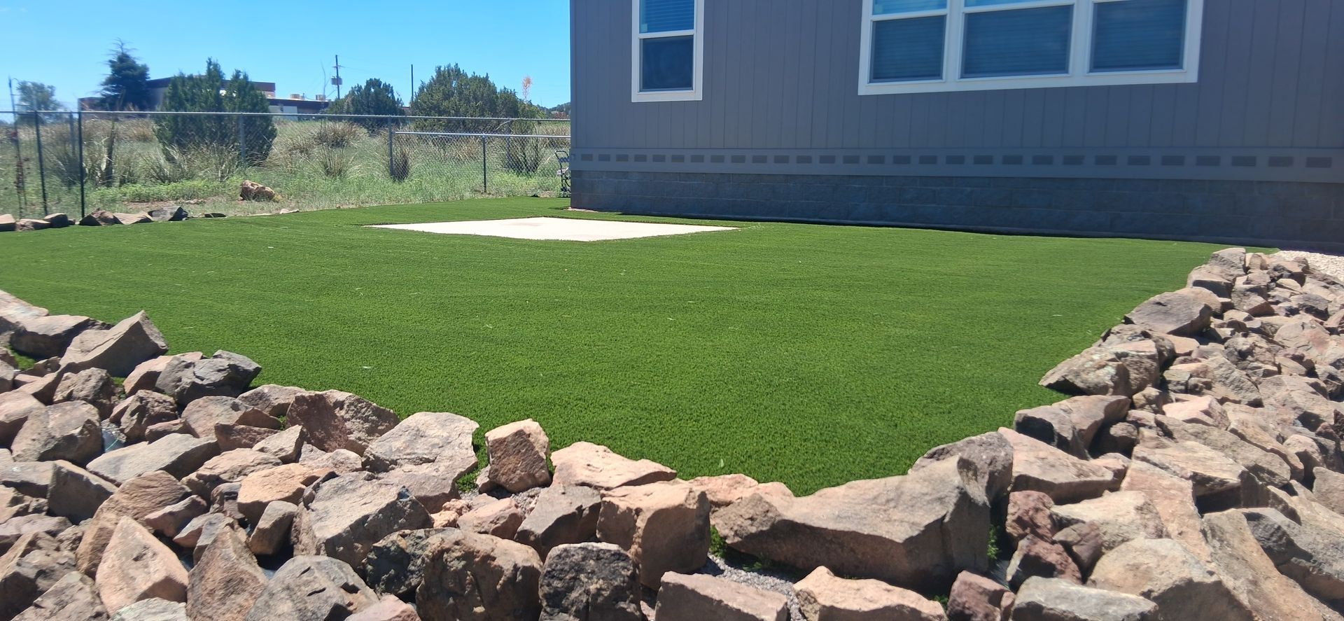 Rock border around a neatly trimmed green lawn beside a house under a clear blue sky