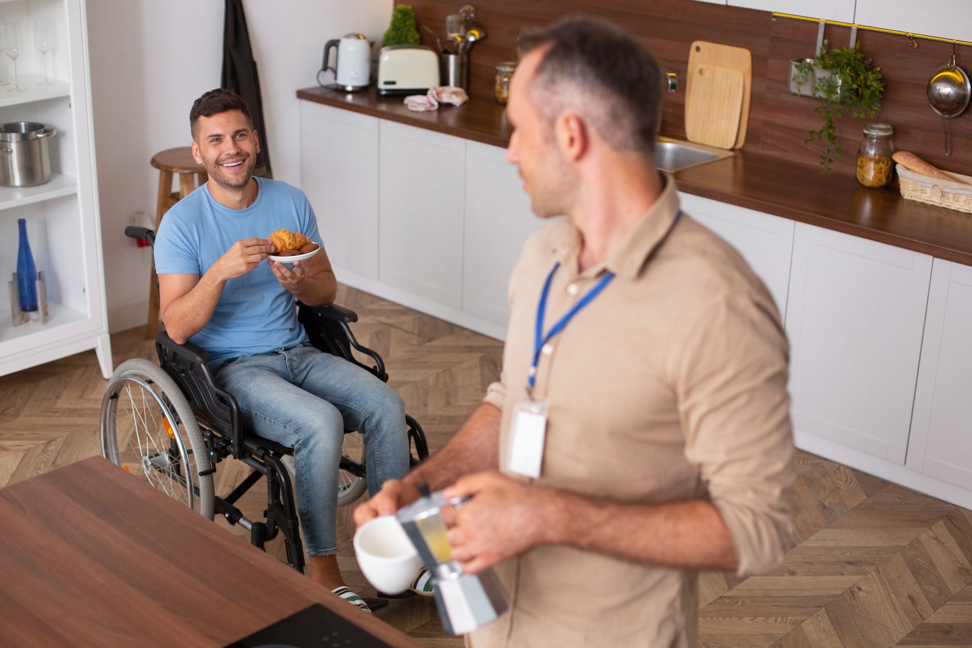 A man in a wheelchair is talking to another man in a kitchen.