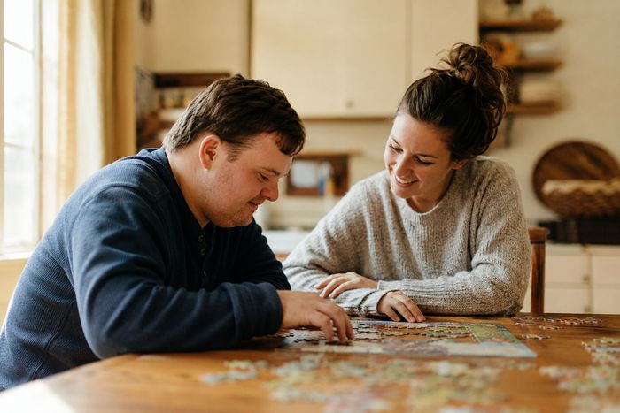 Caregiver supporting an adult with intellectual disabilities during a puzzle activity at home