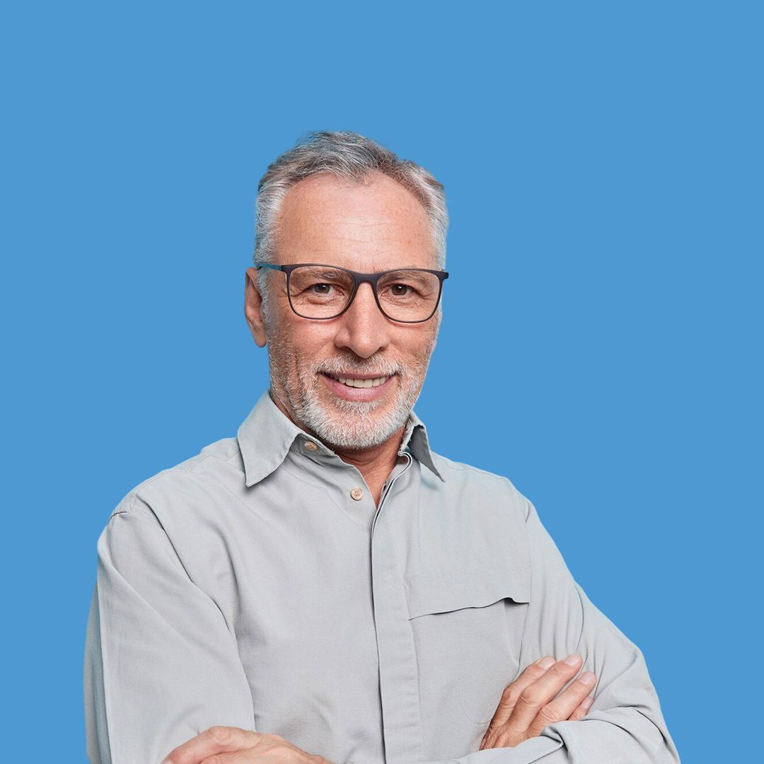 A man wearing glasses and a grey shirt is standing with his arms crossed.