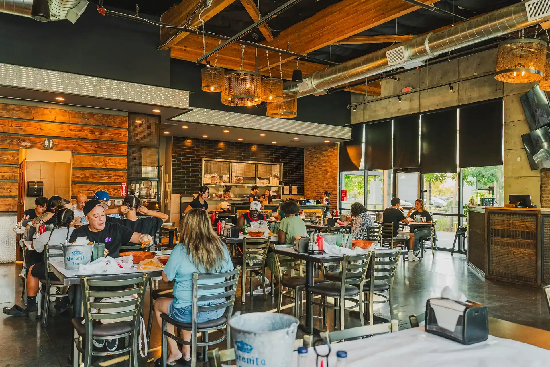 Busy modern restaurant dining room with exposed beams, warm lighting, and people seated at tables