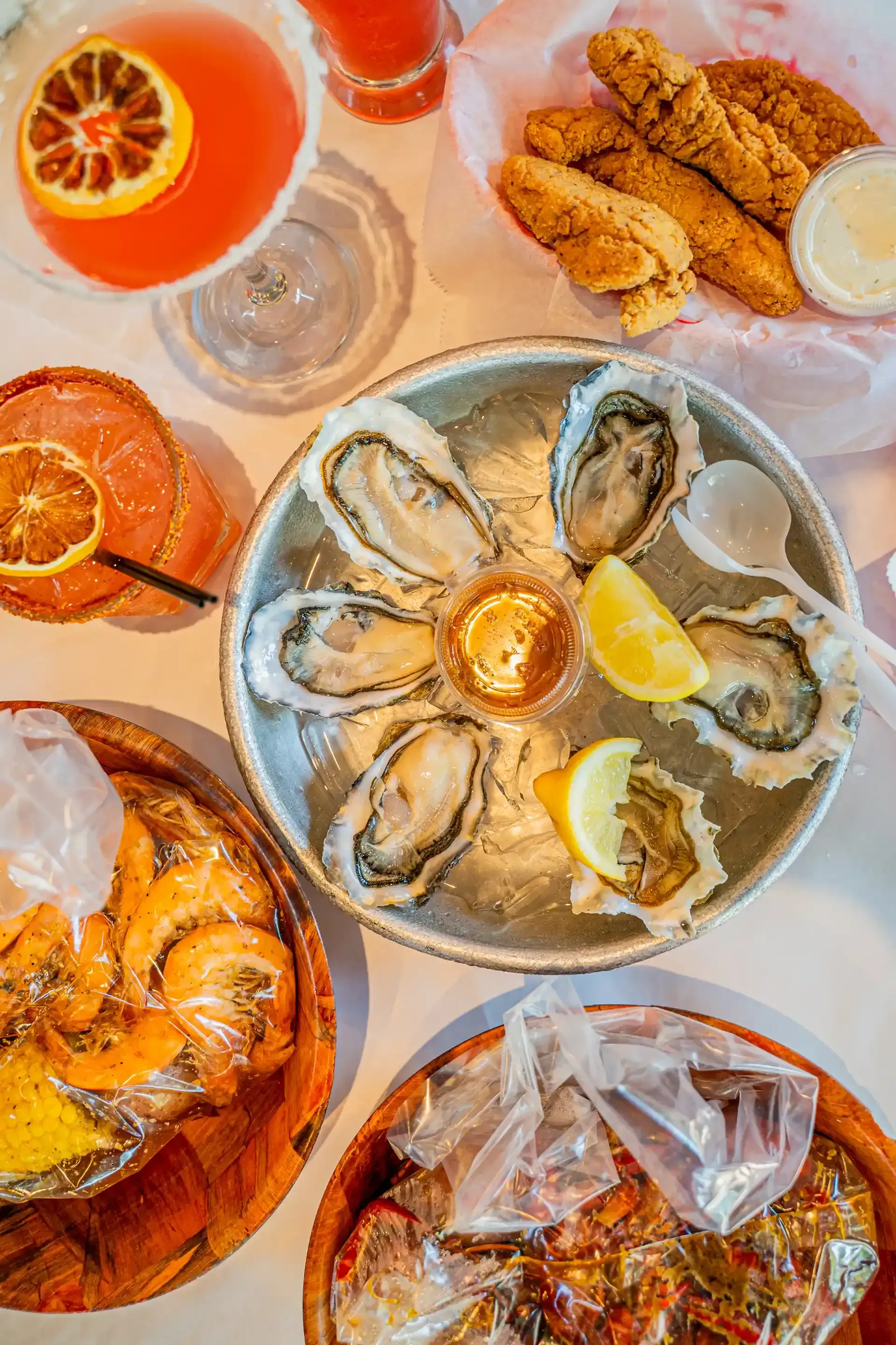 Seafood platter with oysters, shrimp, fried fish, lemon wedges, and orange cocktails on a bright table