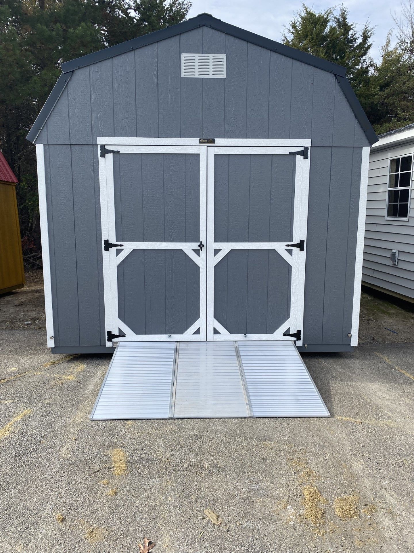 Gray shed with white-trimmed double doors and metal ramp in front.