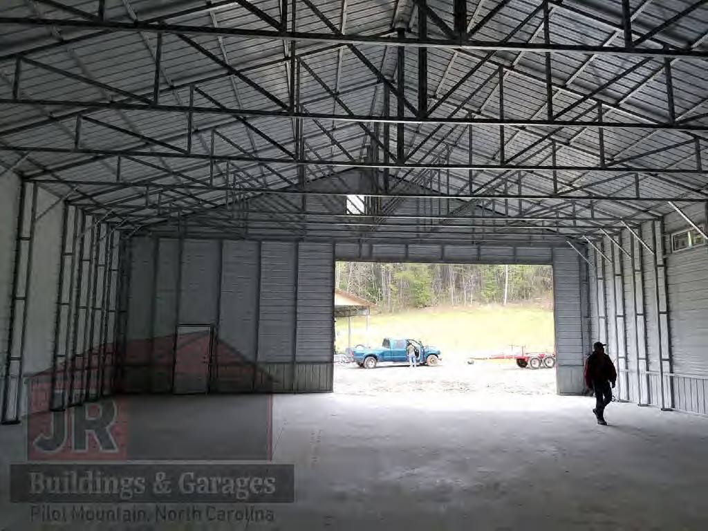 Interior of a metal building with concrete floor and large open door. A person walks toward the outside.