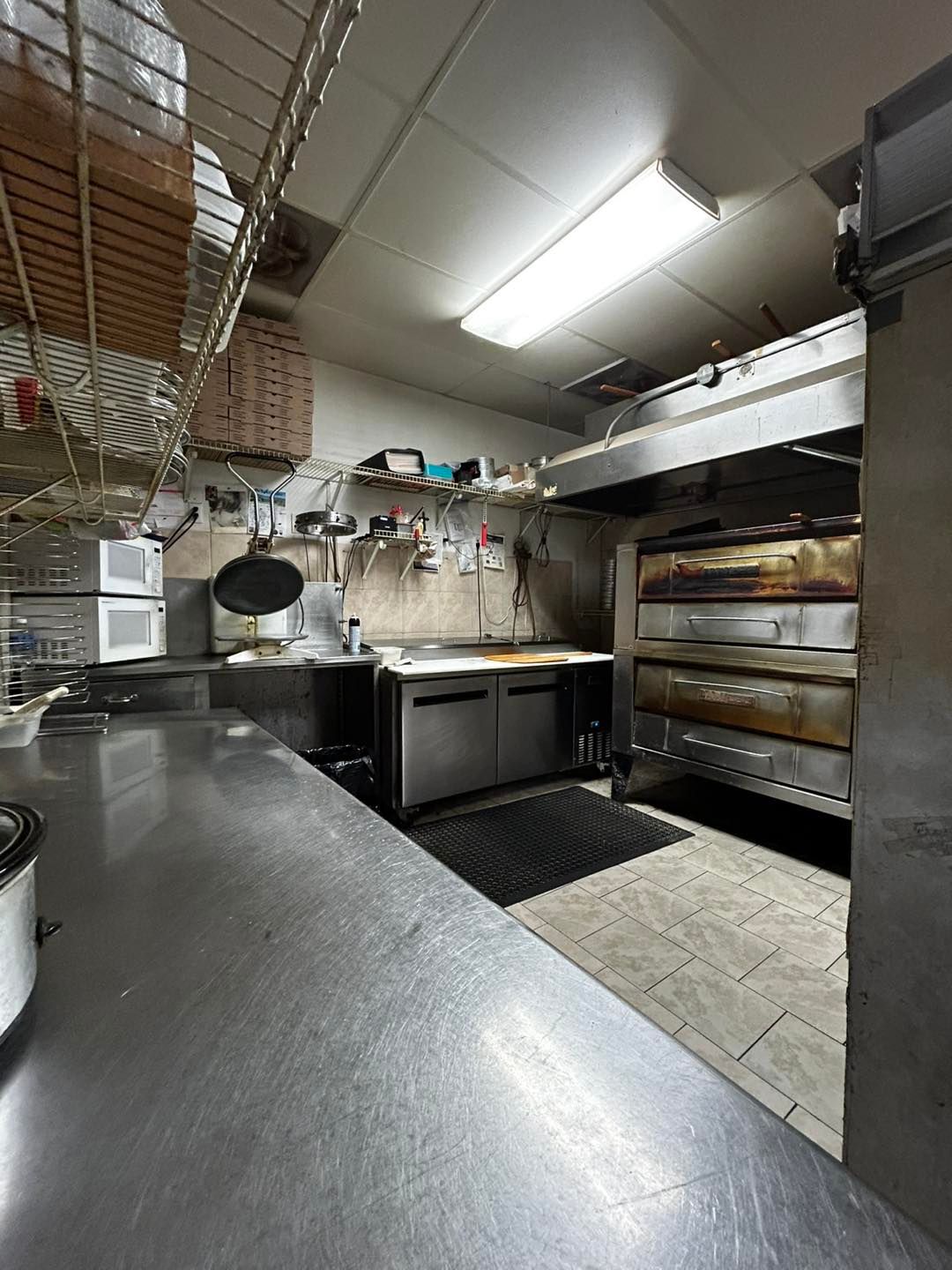 Kitchen interior with pizza ovens, stainless steel counters, and cooking equipment.