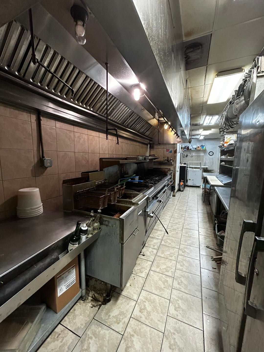 Commercial kitchen interior with stainless steel appliances, tile floor, and overhead ventilation system.