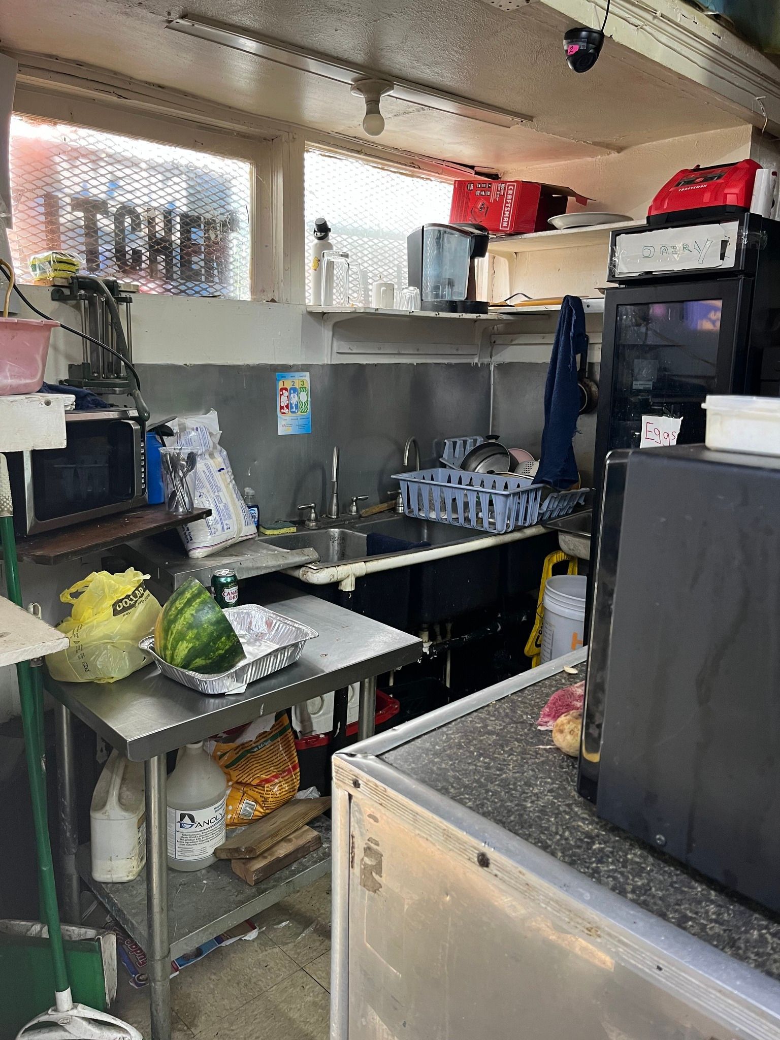 Small, cluttered commercial kitchen with stainless steel counter, microwave, sink, and various appliances.