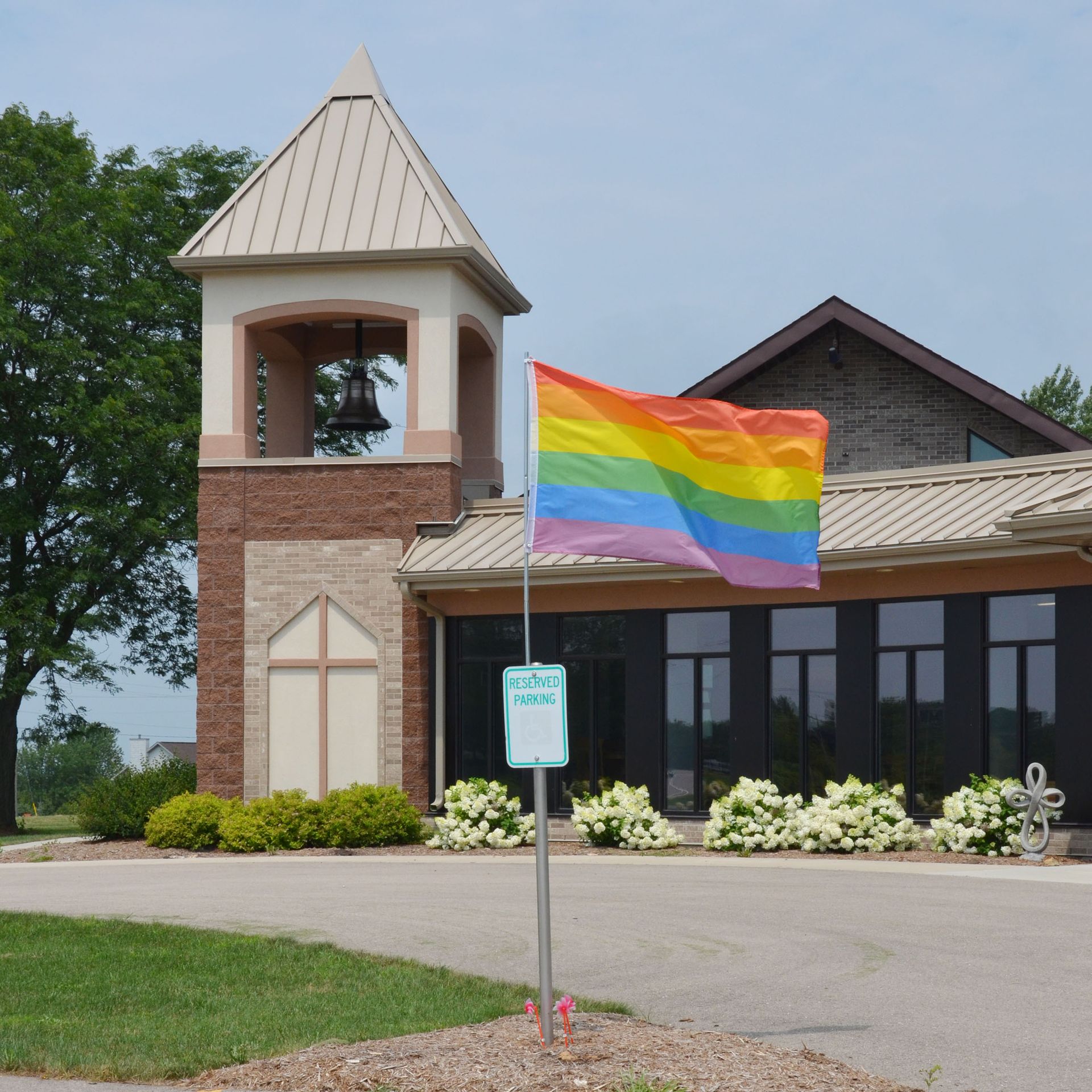 Rainbow flag flies in front of a church building with a bell tower.