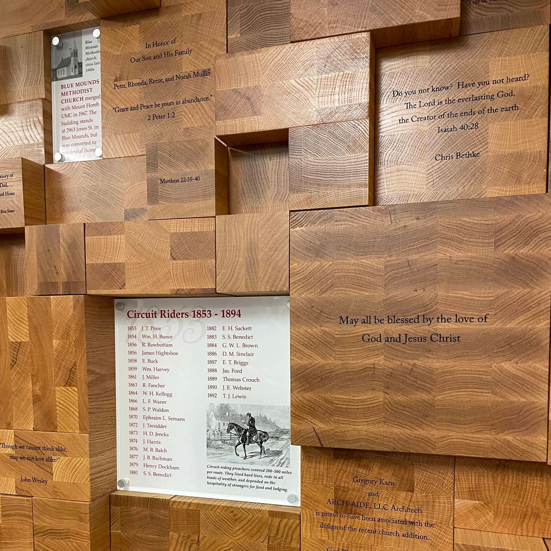 Wooden wall with engraved text and lists, including a framed photo and text.