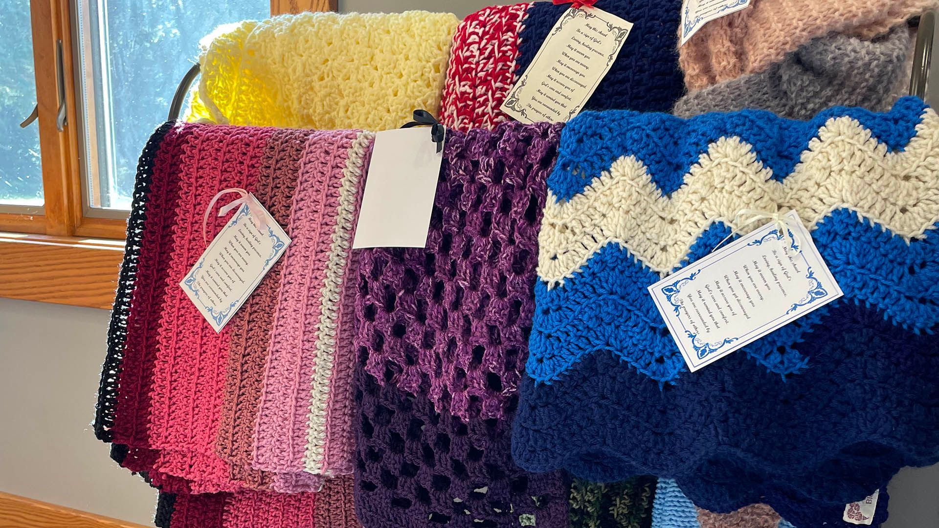 Close-up of colorful crocheted blankets with blessing tags.
