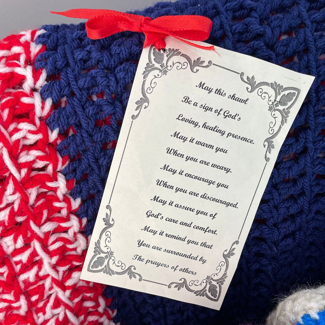 Crocheted red, white, and blue blanket with a tag tied with a red ribbon. Tag reads a prayer.