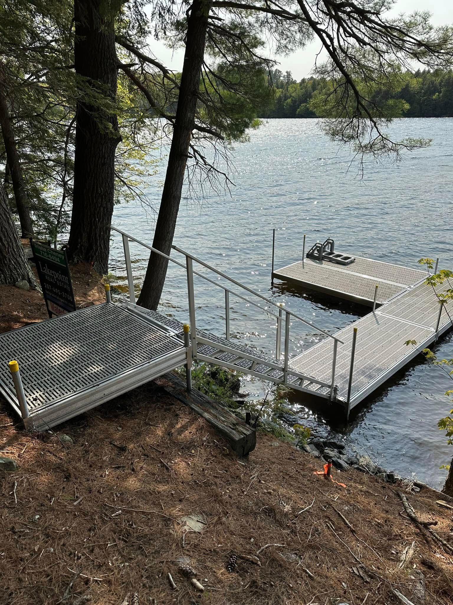 Lakeside dock with metal stairs, bench, and trees along a wooded shoreline.