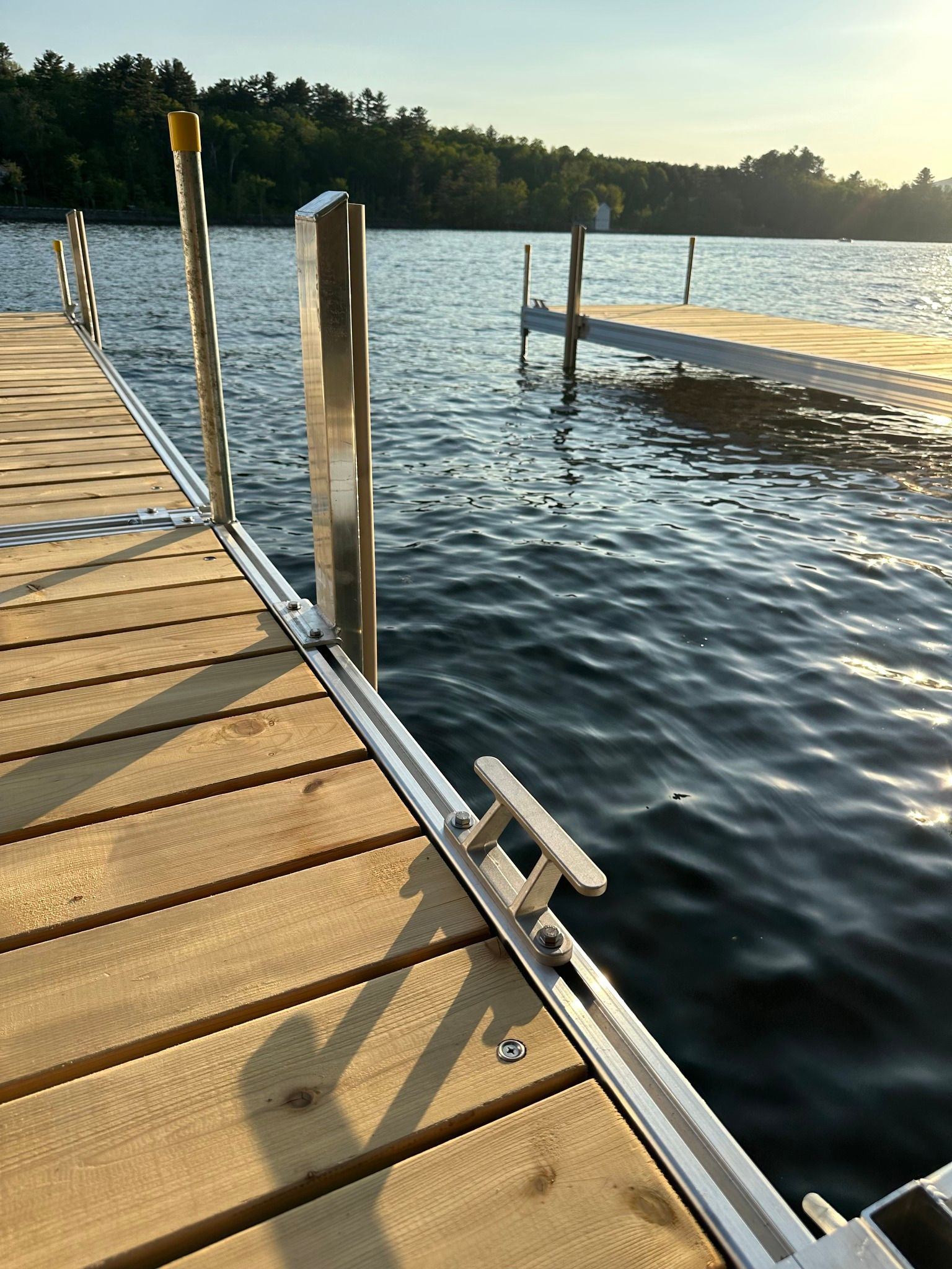 Wooden dock beside a calm lake at sunset, with railings and a low floating platform.