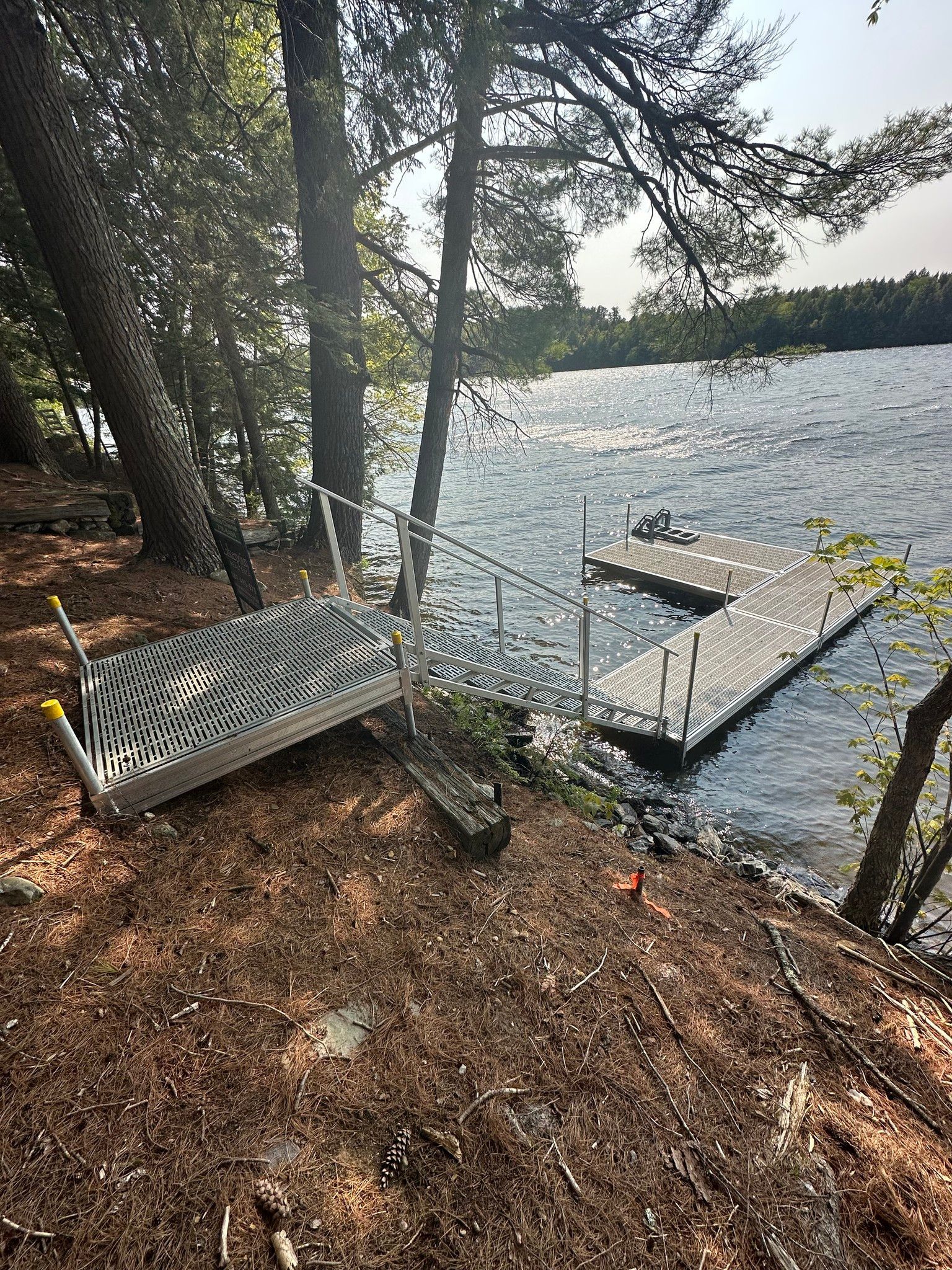 Lakeside dock with white bench, trees, and choppy water on a wooded shore
