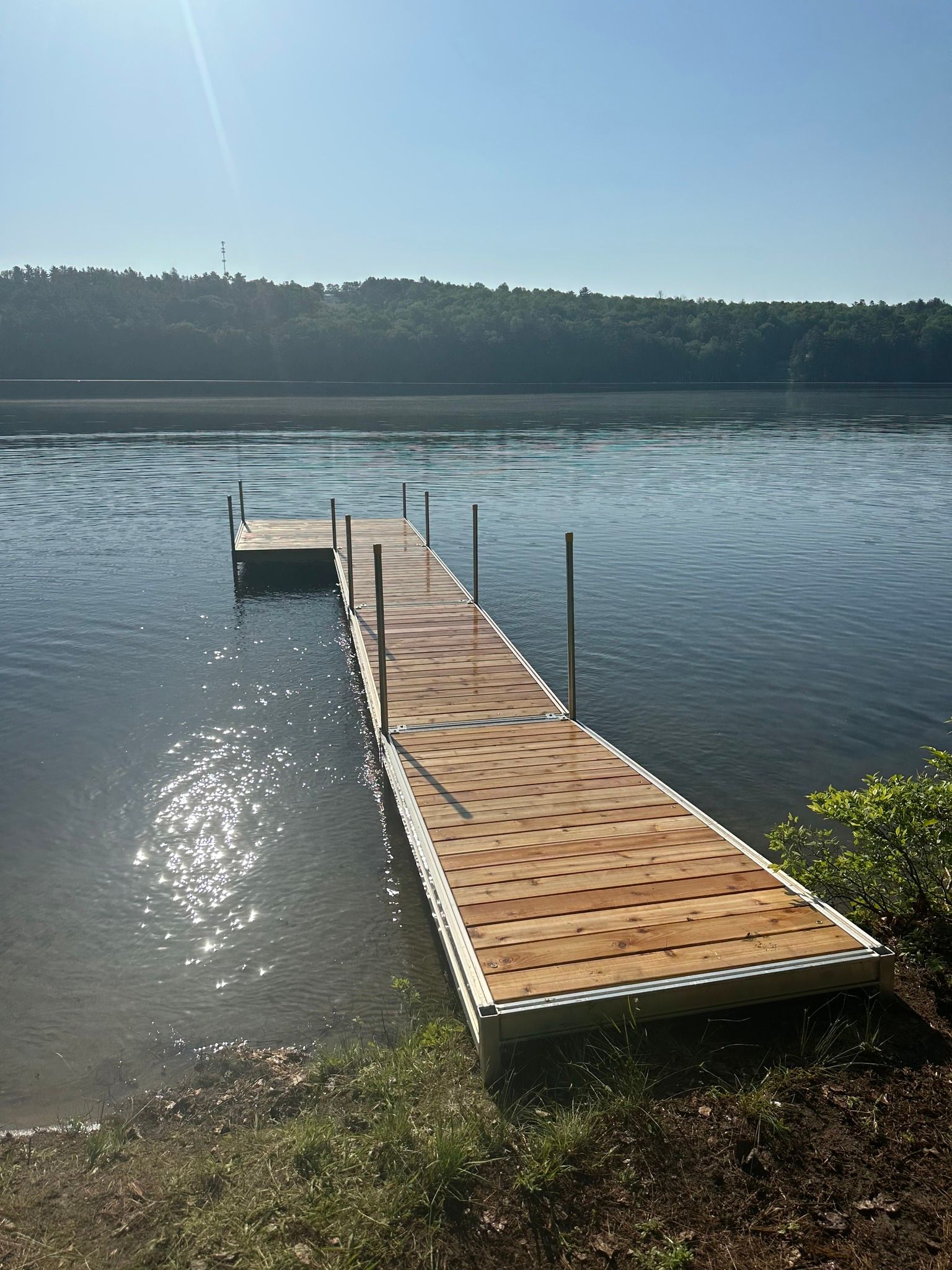 Wooden dock extending into a calm lake under a clear sky, with forested shoreline in the distance.