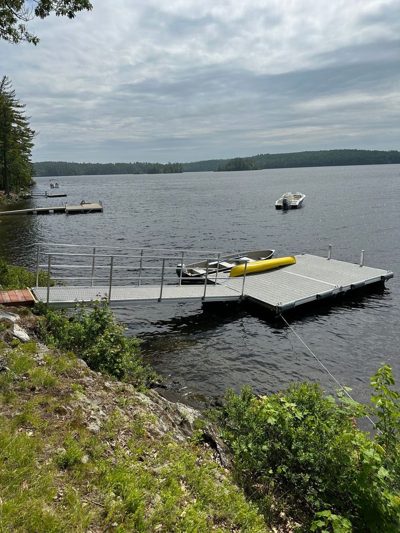 Floating dock on a lake with a yellow kayak, small boat, and cloudy sky above.