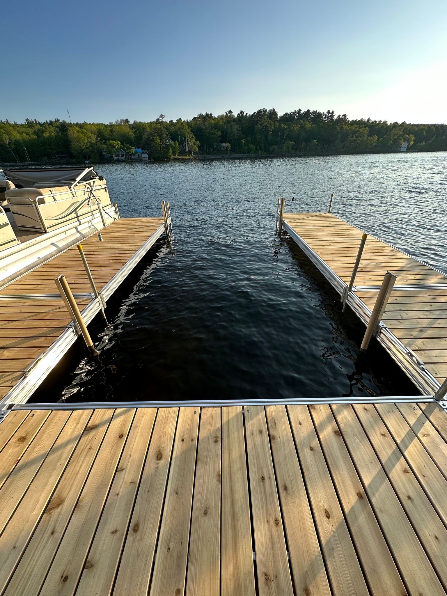 Wooden dock with steps into a lake, framed by calm water and a tree-lined shore at sunset.
